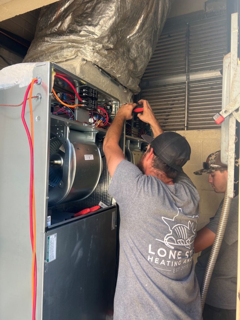 Two Lone Star technicians servicing the internal wiring and components of an open indoor air handler unit.