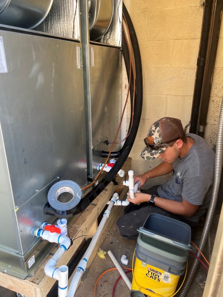 A Lone Star technician kneeling to install white PVC drainage piping for a pair of indoor HVAC units.