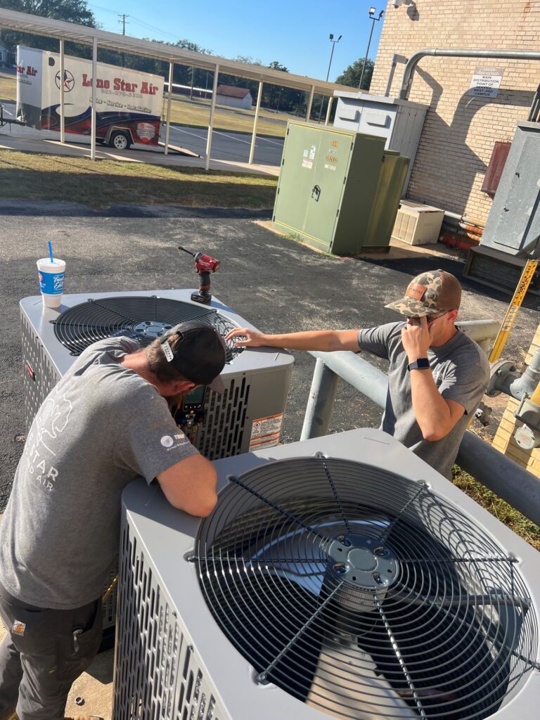 Two Lone Star Air technicians inspecting and working on new outdoor air conditioning units.